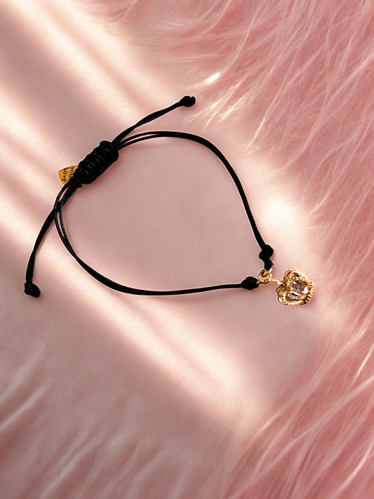 Black cord bracelet with gold crown charms on a pink fabric background